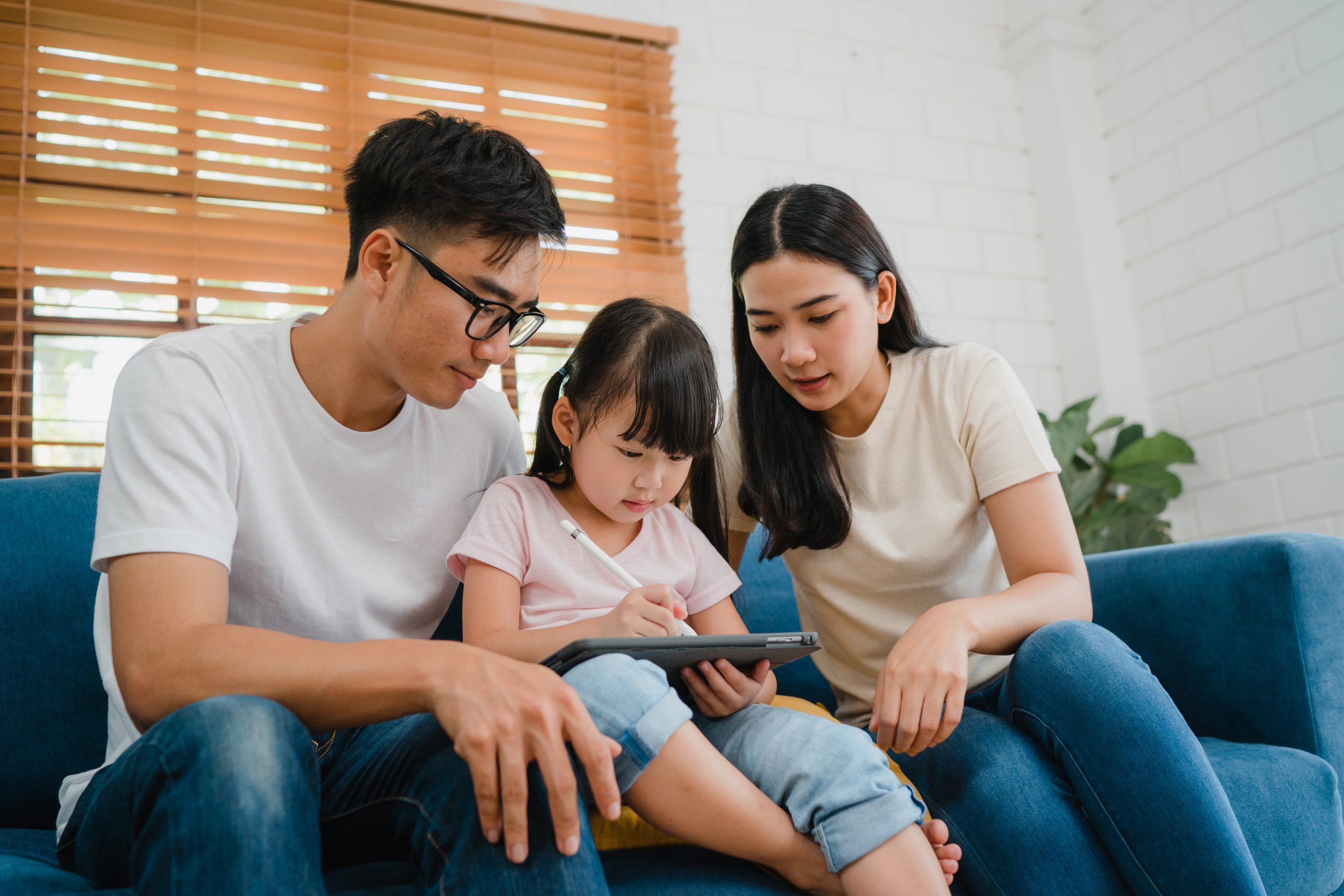 happy asian family dad mom daughter using computer tablet technology sitting sofa living room house Happy Asian family dad, mom and daughter using computer tablet technology sitting sofa in living room at house. Self-isolation, stay at home, social distancing, quarantine for coronavirus prevention.