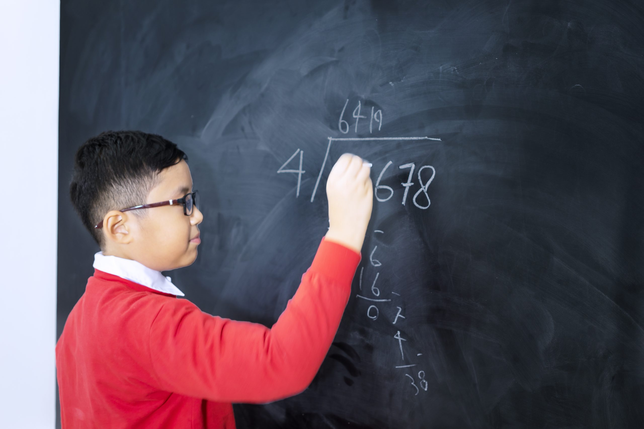 side view adorable boy solving calculations Side view of an adorable Asian boy wearing school uniform while solving a division calculation in a classroom