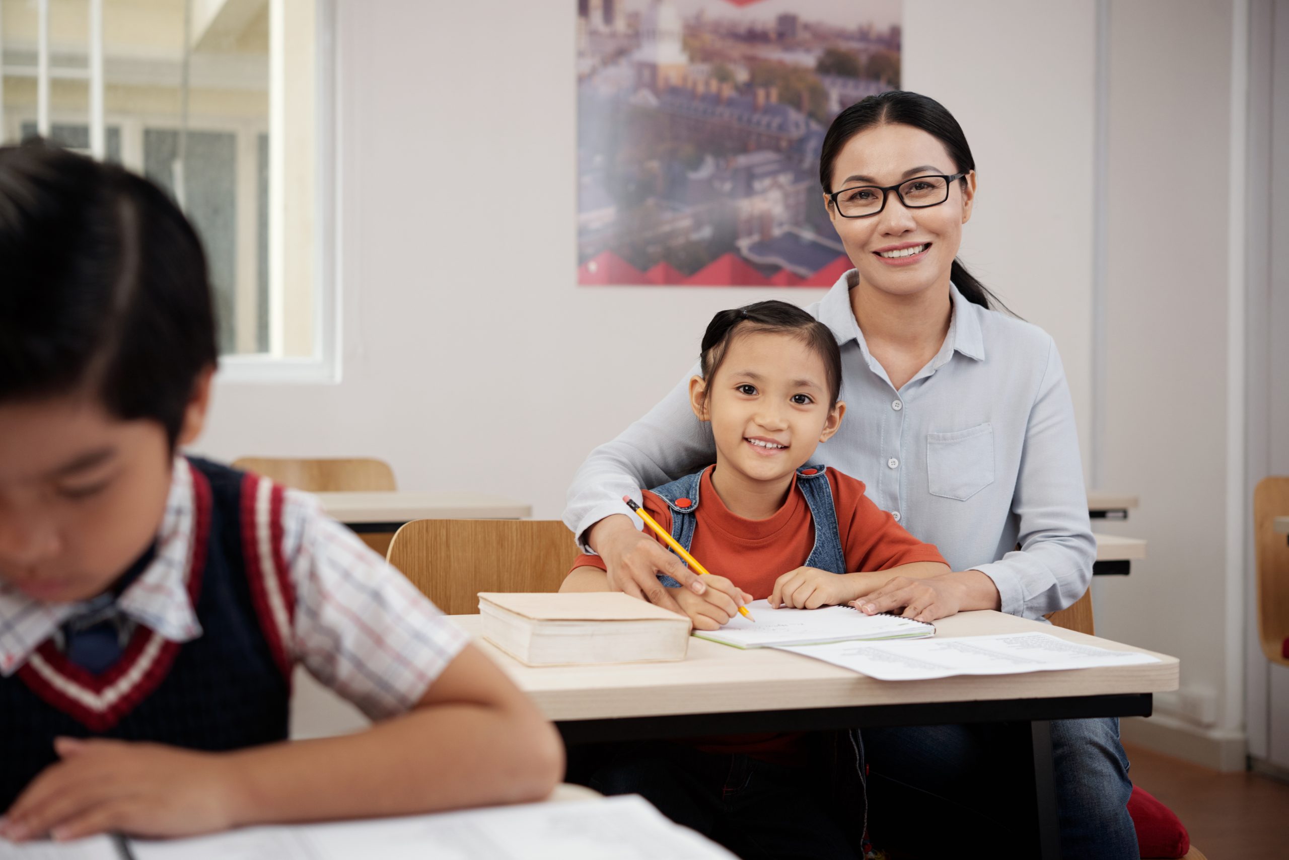 teacher helping student Cheerful Vietnamese teacher helping little girl with difficult task