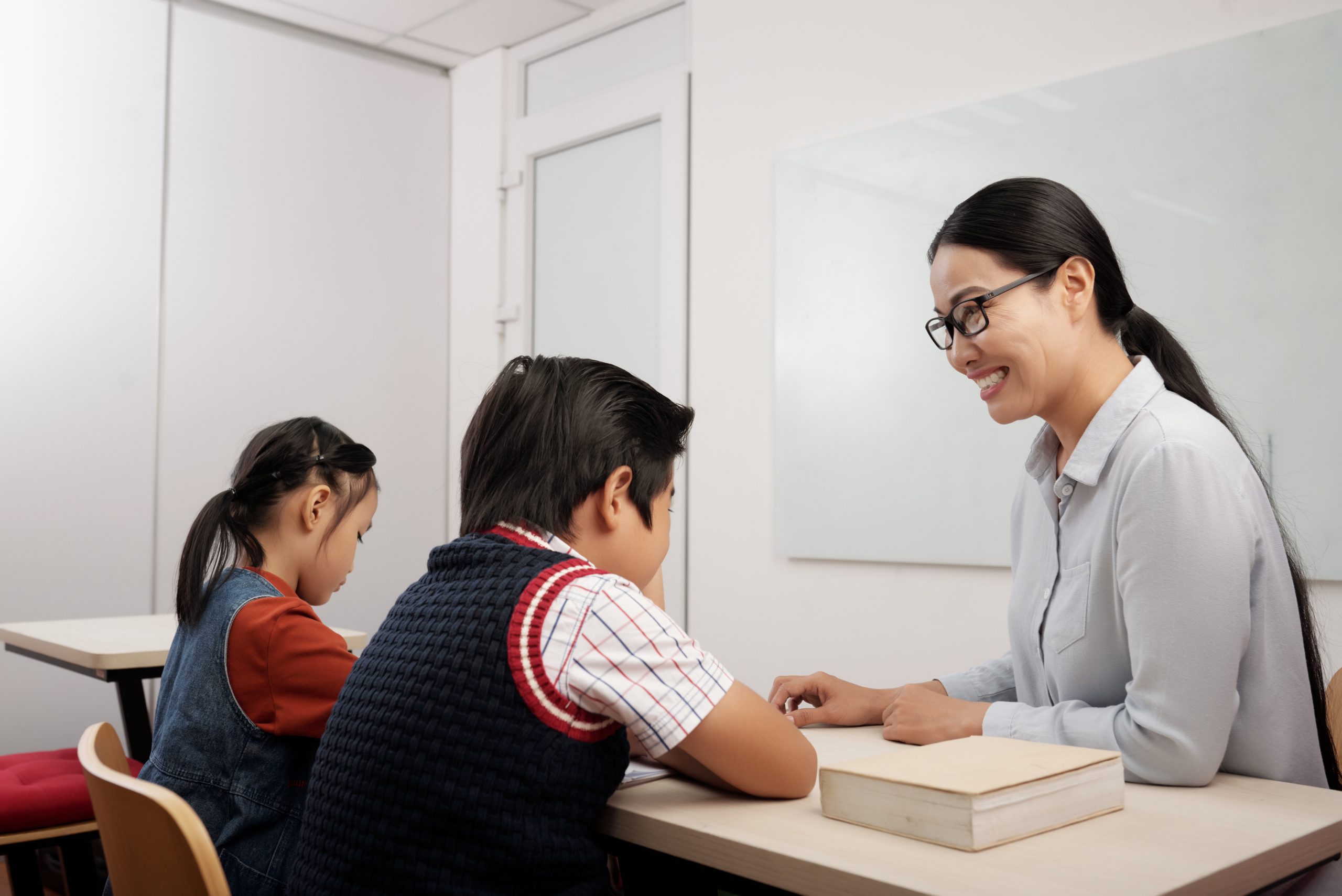 two asian kids sitting classroom smiling teacher glasses talking boy two asian kids sitting classroom smiling teacher glasses talking boy